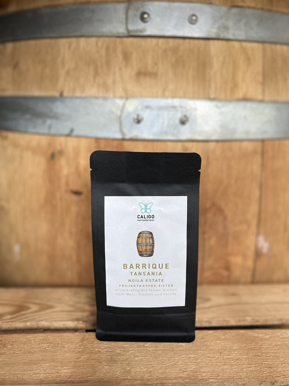 Barrique Tansania Ngila Estate Projektkaffee der Caligo Kaffeerösterei in einer schwarzen Kaffeetüte vor einem Weinfass