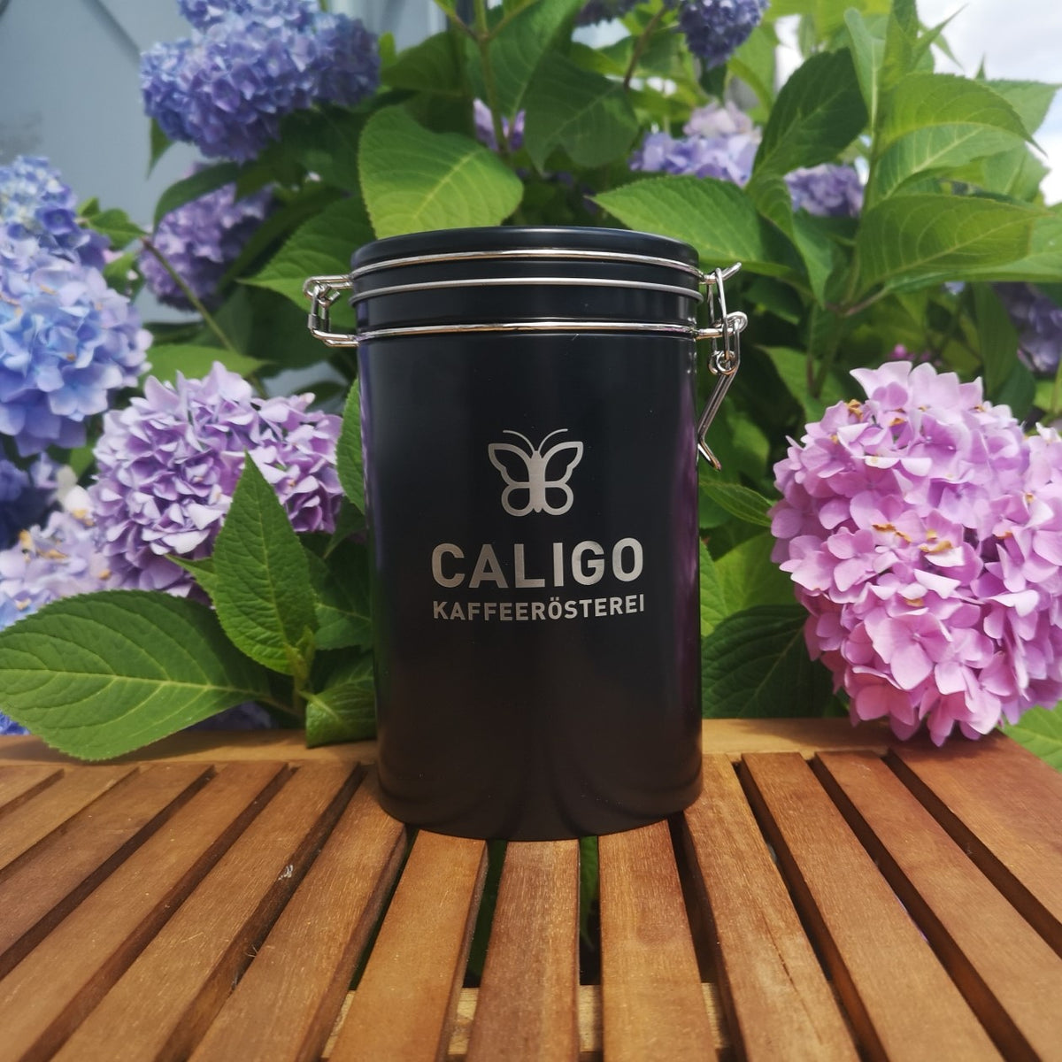 gravierte Caligo Kaffeerösterei Kaffeedose schwarz auf Holztisch vor Hortensie